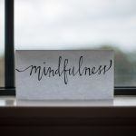Weißes Kärtchen mit handschriftlichem Zug "mindfulness", vor unscharfem Fenster.